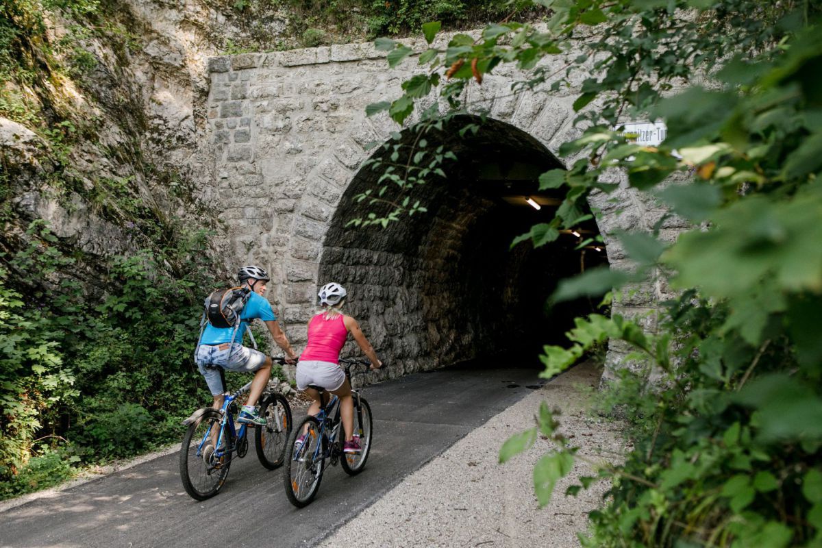 2 Radfahrer fahren richtung Eingangsportal des Tunnels.