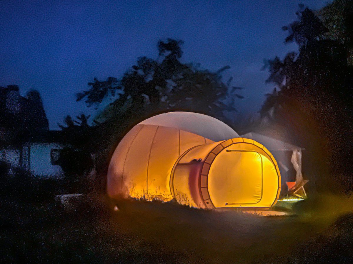 Ein Bubbletent: Kuppelförmiges Zelt mit viel Ausblick nach oben in den Sternenhimmel, hier von innen beleuchtet bei Nacht.
