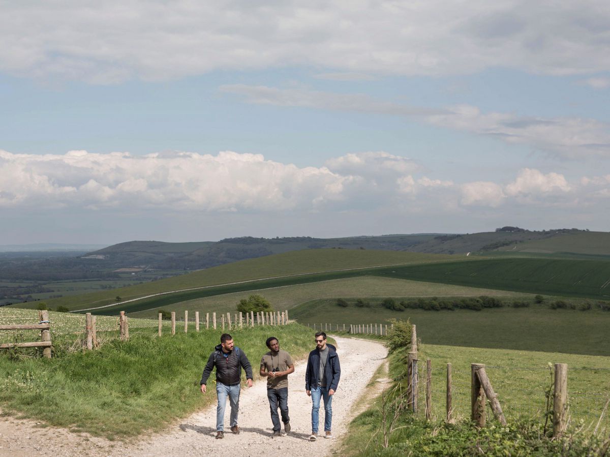 Drei Wanderer auf dem South Downs Way: Ein Wanderweg zwischen Weidezäunen durch die sanften grünen Hügel.