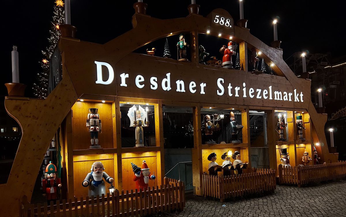 Dresdner Striezelmarkt in der Nacht. Der Eingang ist wie ein riesiger Schwibbogen mit beleuchteten Nischen gestaltet. In den Nischen sind typische Figuren aus dem Erzgebirge (Engel, Nussknacker).