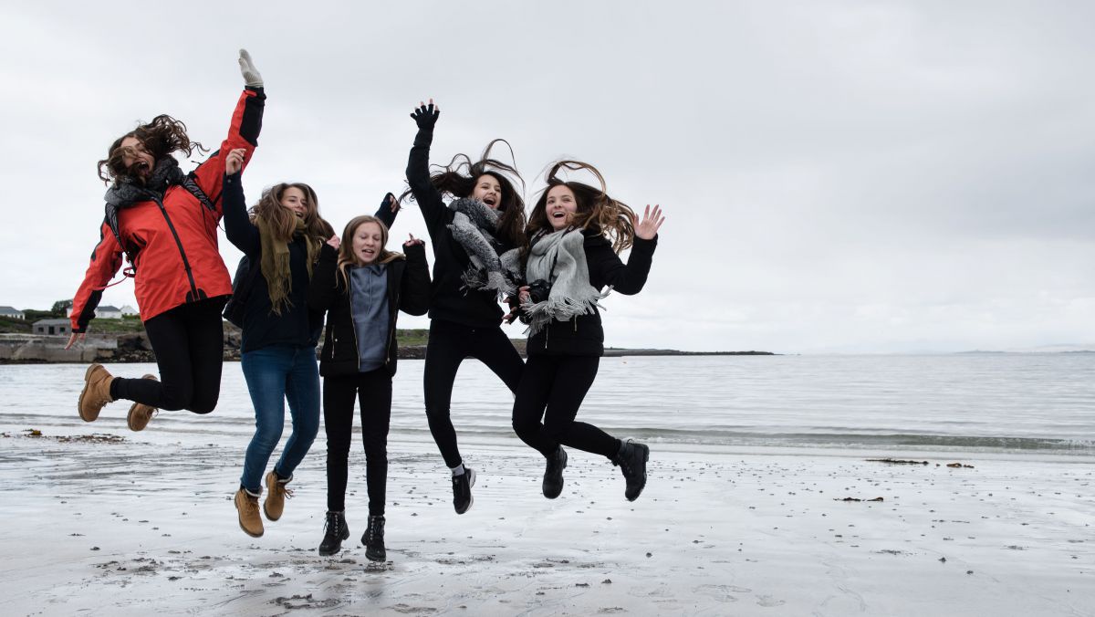5 Mädchen springen am Strand in Irland in die Höhe.