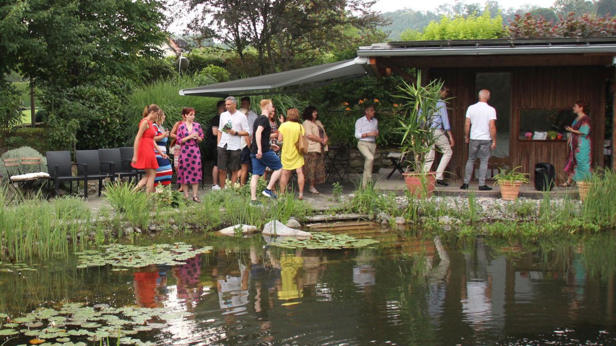 Gruppe von Menschen im Garten mit großem Teich im Vordergrund.