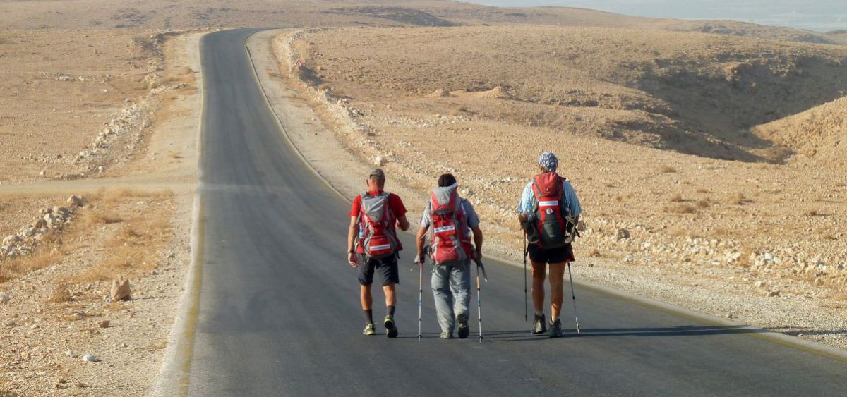 Die drei Wanderer auf einer leeren Straße in der Wüste.
