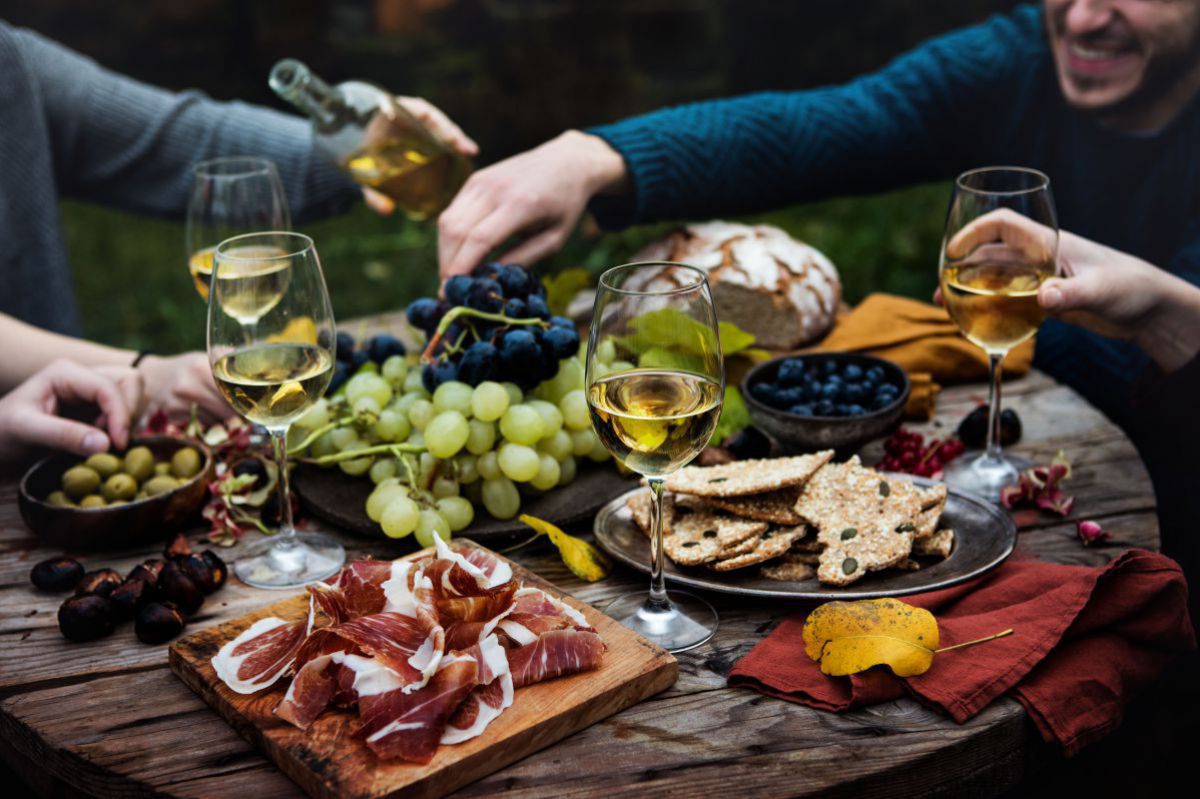 Tisch gedeckt mit Oliven, Speck, Weintrauben, Wein, Brot.