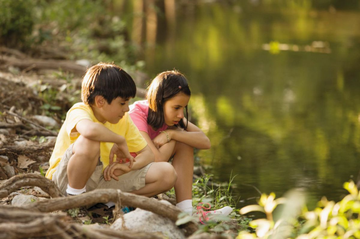 Kinder hocken staunend am Ufer eines Flusses.