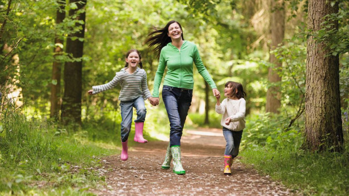 Frau schlendert fröhlich mit 2 Mädchen durch den Wald.