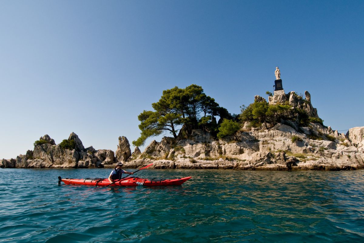 Paddler mit Felseninsel im Hintergrund, auf dem Fels steht eine steinerne Statue.