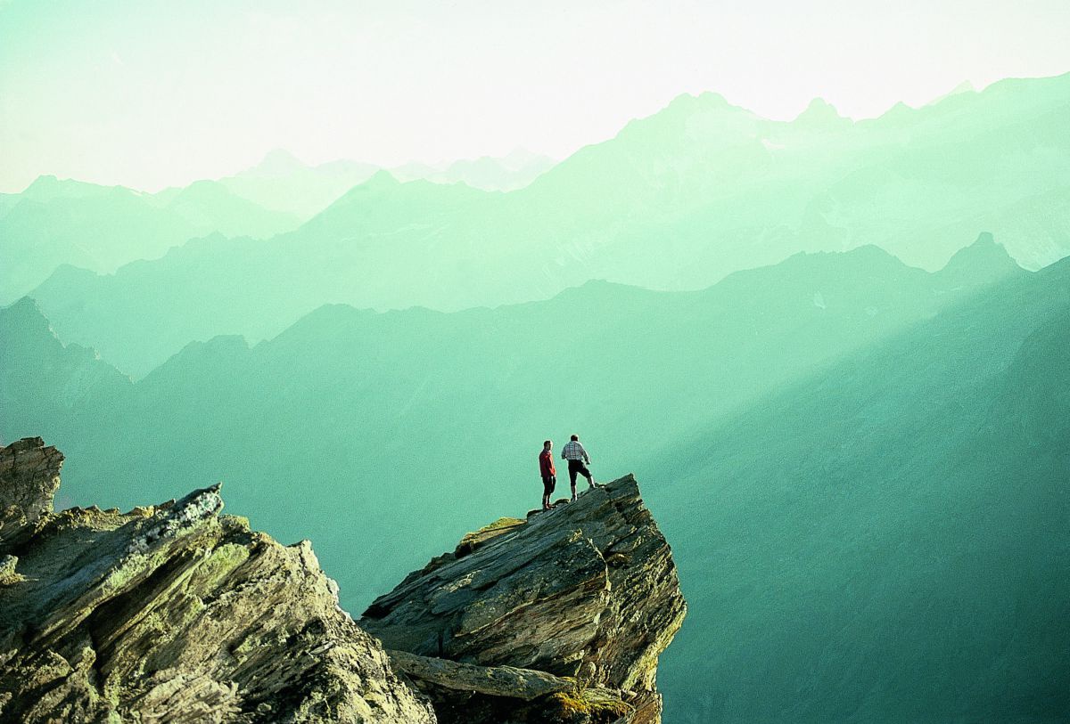 2 Männer auf einem Felsvorsprung in den Bergen.