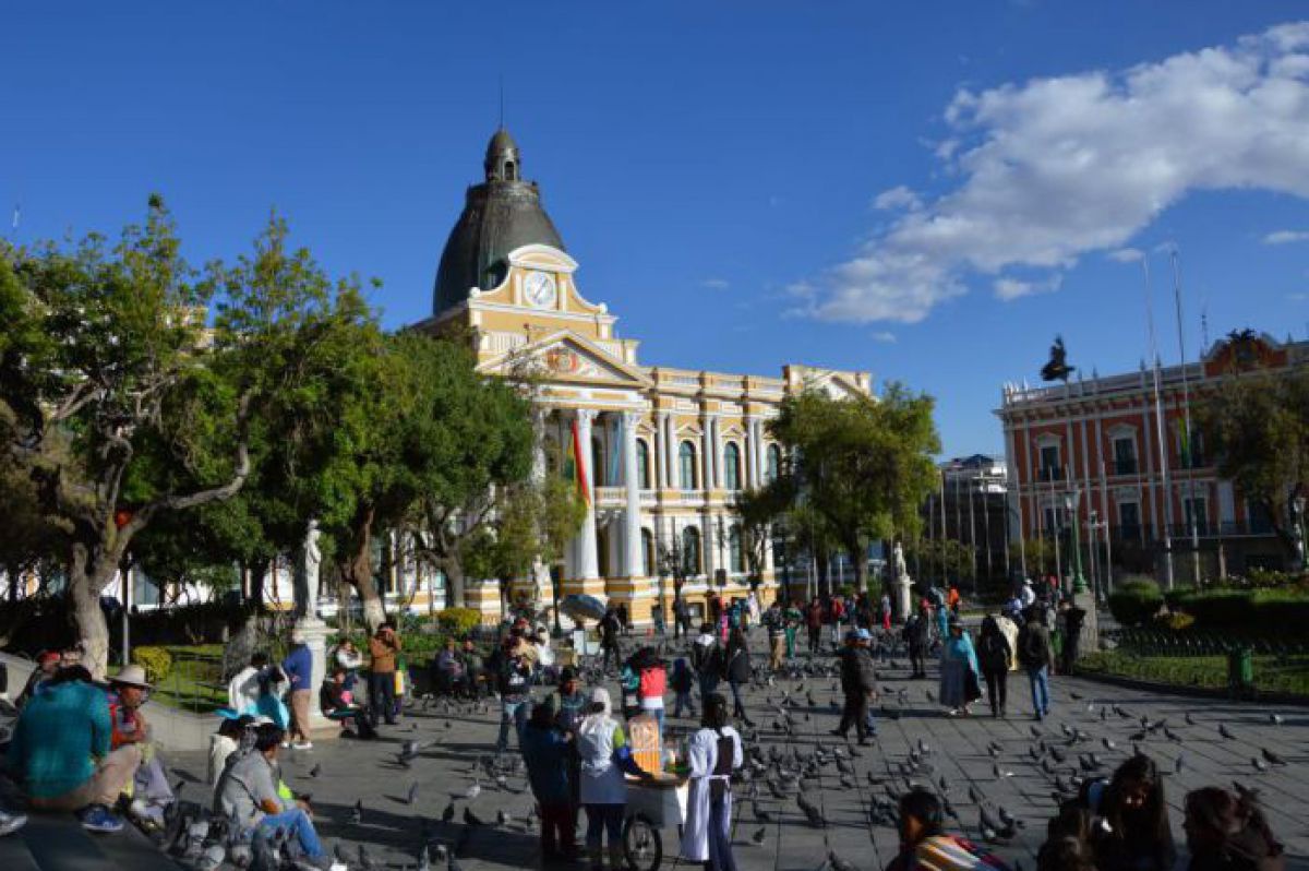 Plaza Morillo in La Paz - viele Menschen und noch mehr Tauben, im Hintergrund ein gelbes Gebäude mit Säuleneingang, Turmuhr und Kuppel.