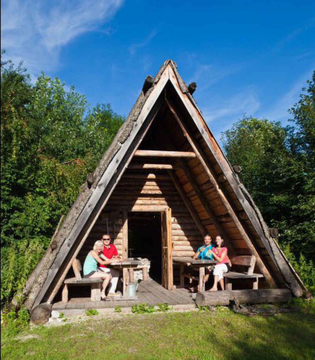 Dreieckige Holzhütte, auf der Terasse sitzen einige Gäste.