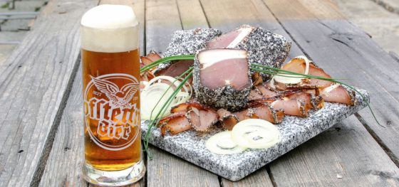 Ein Krügerl Bier und eine Speckjause auf einer Steinplatte.