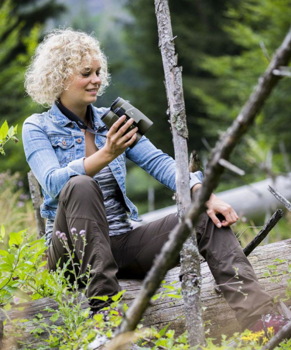 Nina Schönemann mit Feldstecher auf einem liegenden Baumstamm sitzend.