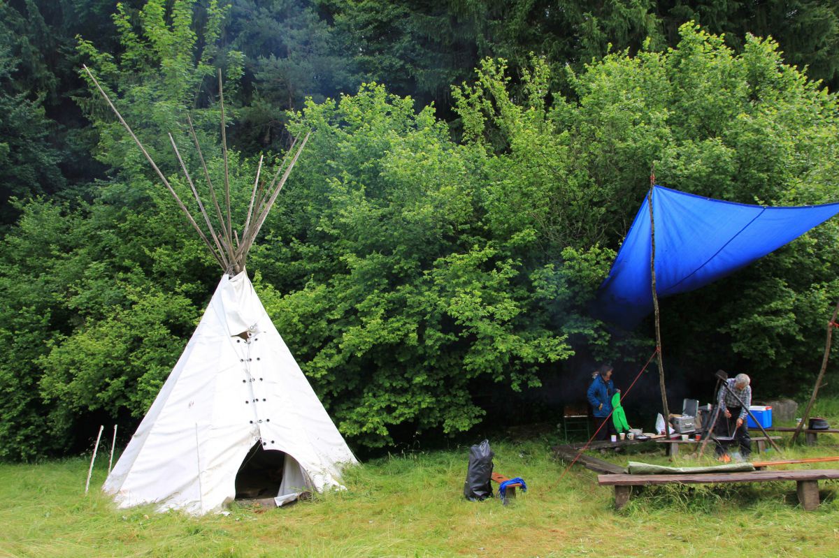 Tipi und Lagerfeuerstelle am Waldrand.