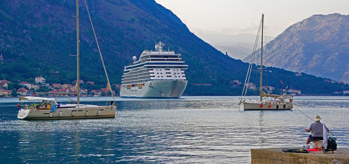 Kreuzfahrtschiff in der Bucht von Kotor, davor 2 kleine Segelschiffe und ein Angler.