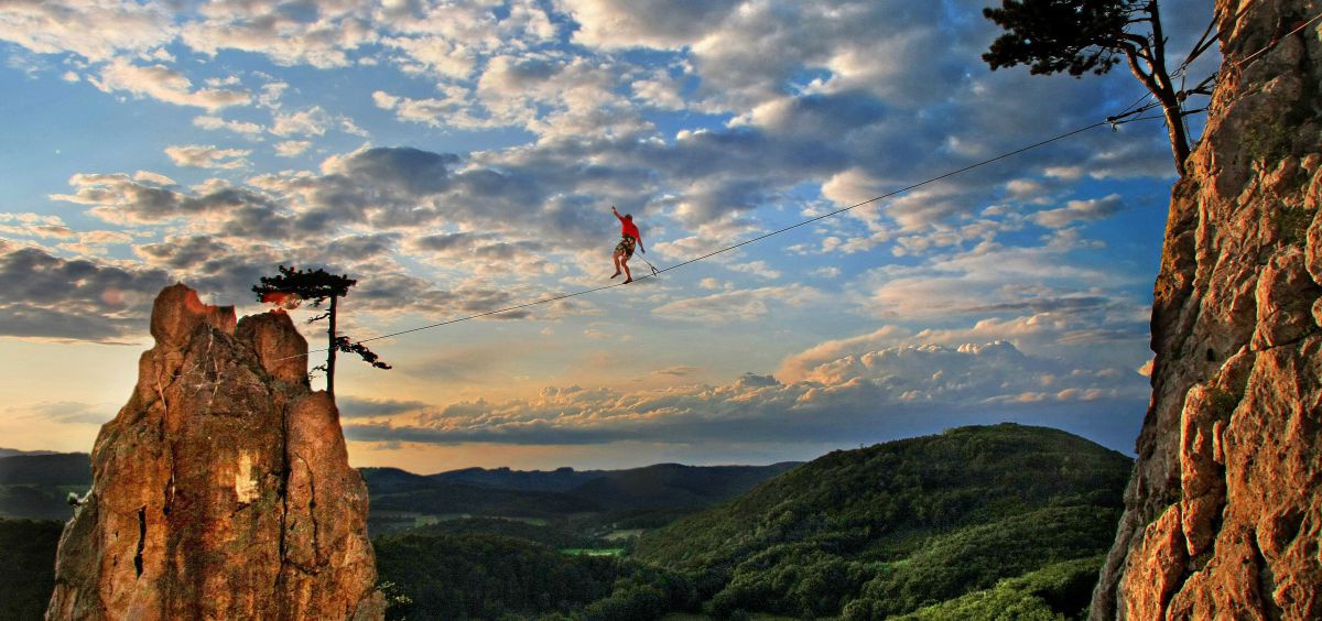 Mann balanciert auf einer Slackline in schwindelerregender Göhe von einem Felsen zum anderen.