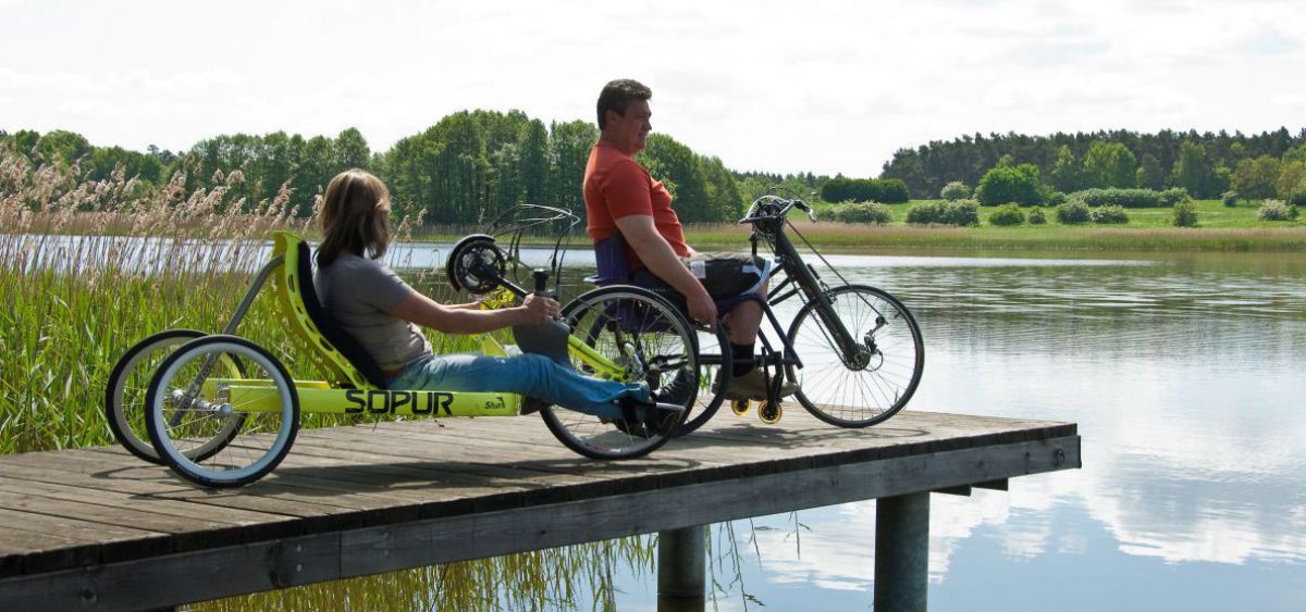 2 Handbiker auf einem Steg am See.