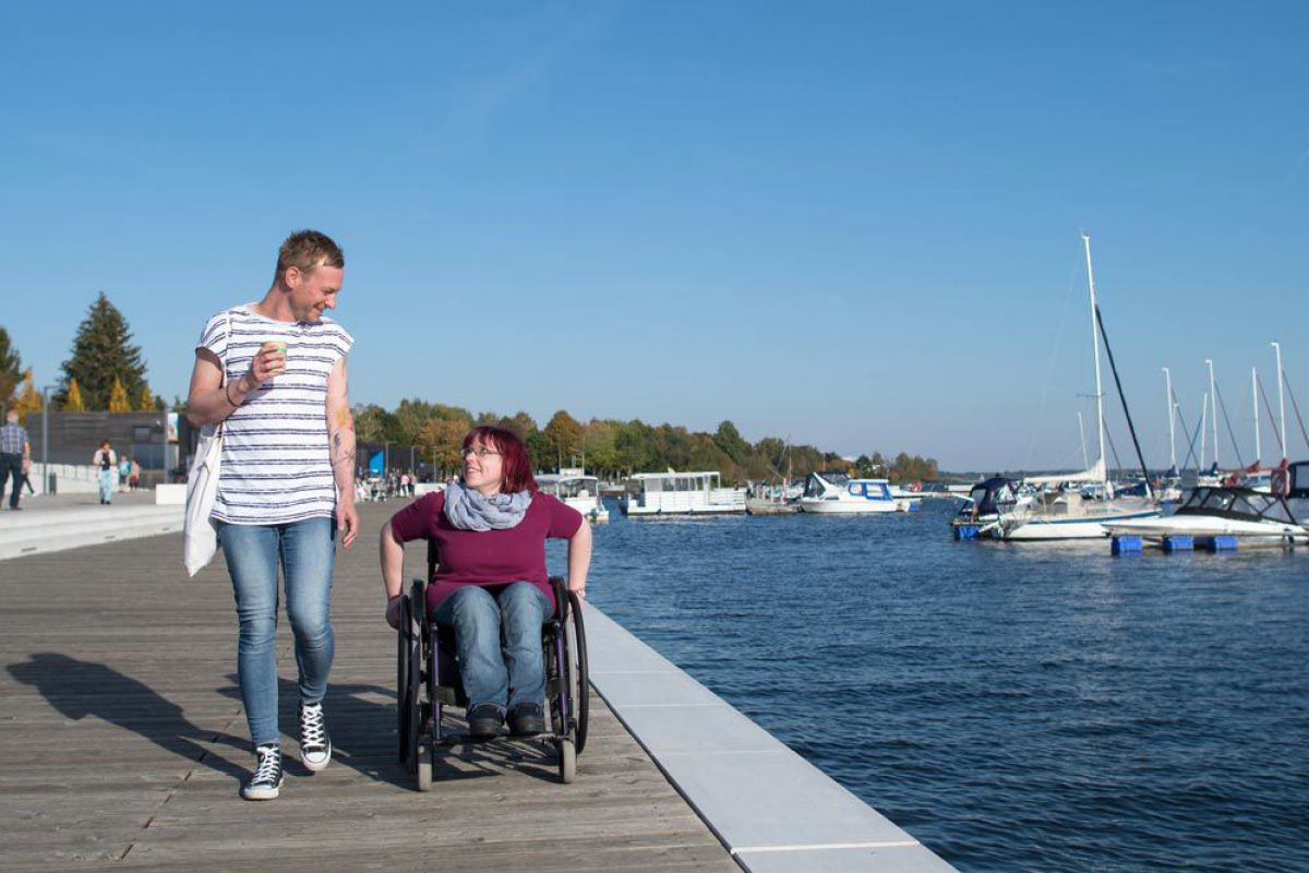 Mann und Frau im Rollstuhl an der Hafenpromenade.