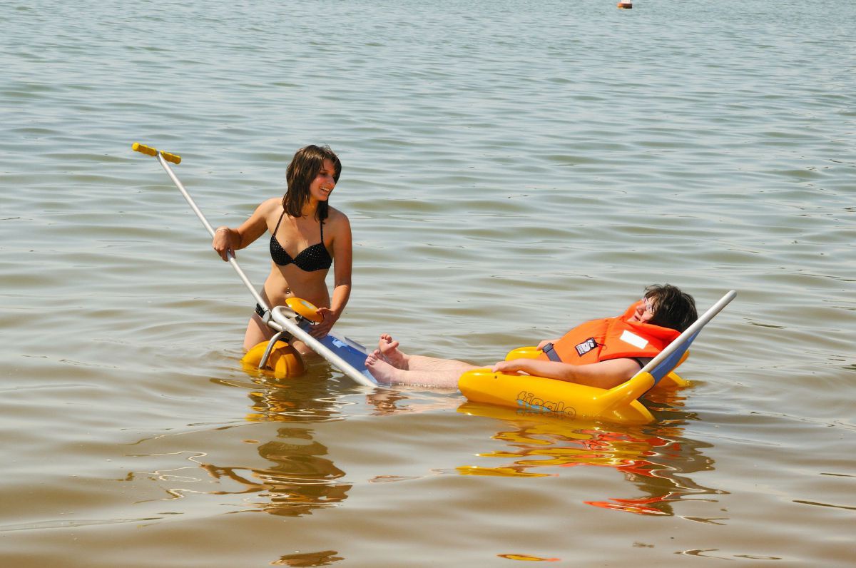 2 Frauen im Wasser, eine sitzt in einem schwimmenden Rollstuhl.enland_und_partner-2