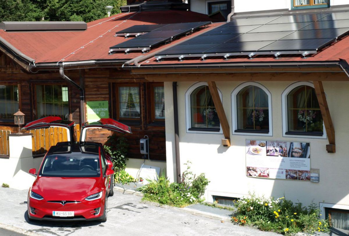 Roter Tesla an der Stromladestelle vor dem Hotel mit PV-Anlage am Dach.
