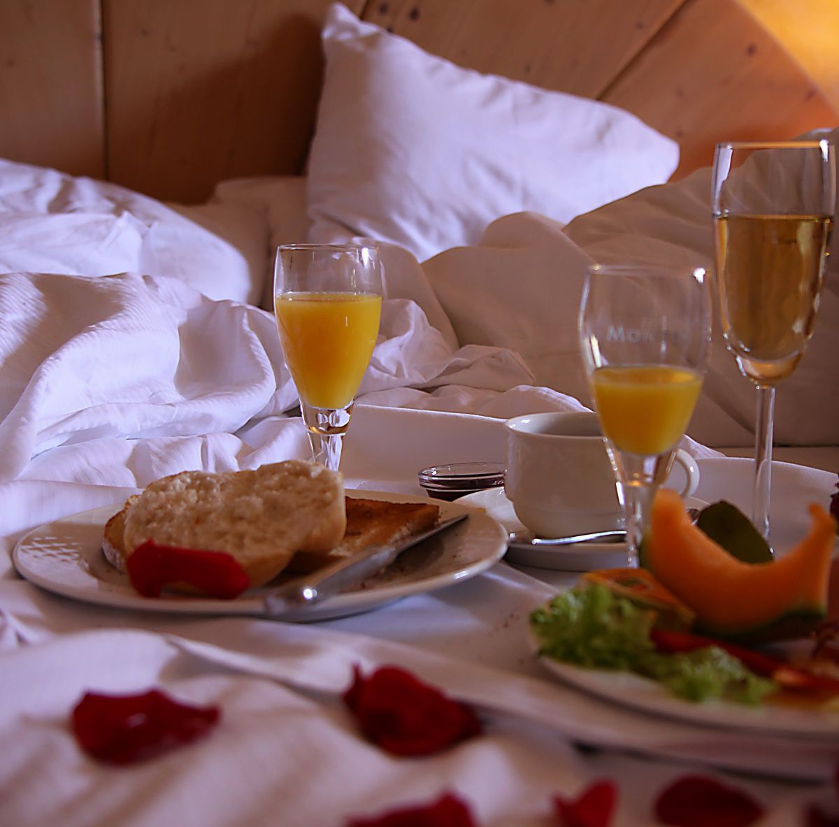 Teller mit Semmel, Gläser mit Orangensaft ein Glas Sekt, Rosenblätter im Bett.