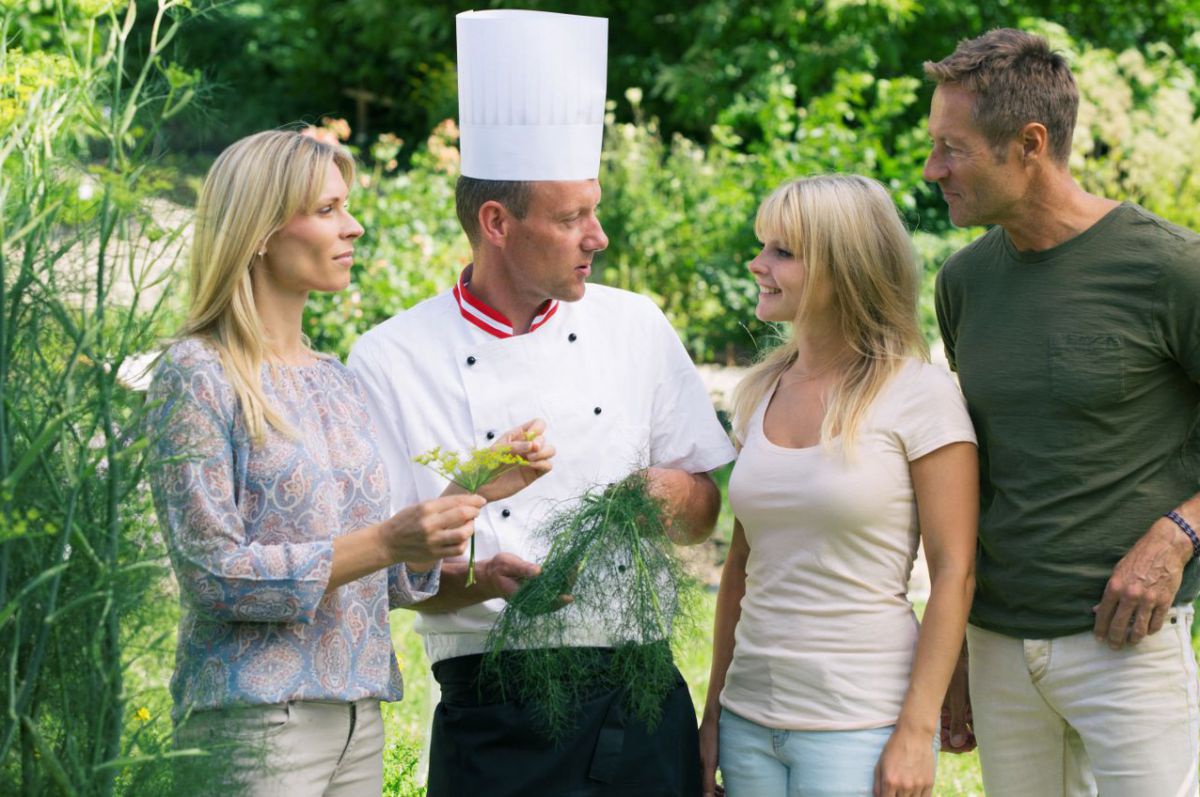 Koch mit Gästen im Kräutergarten.