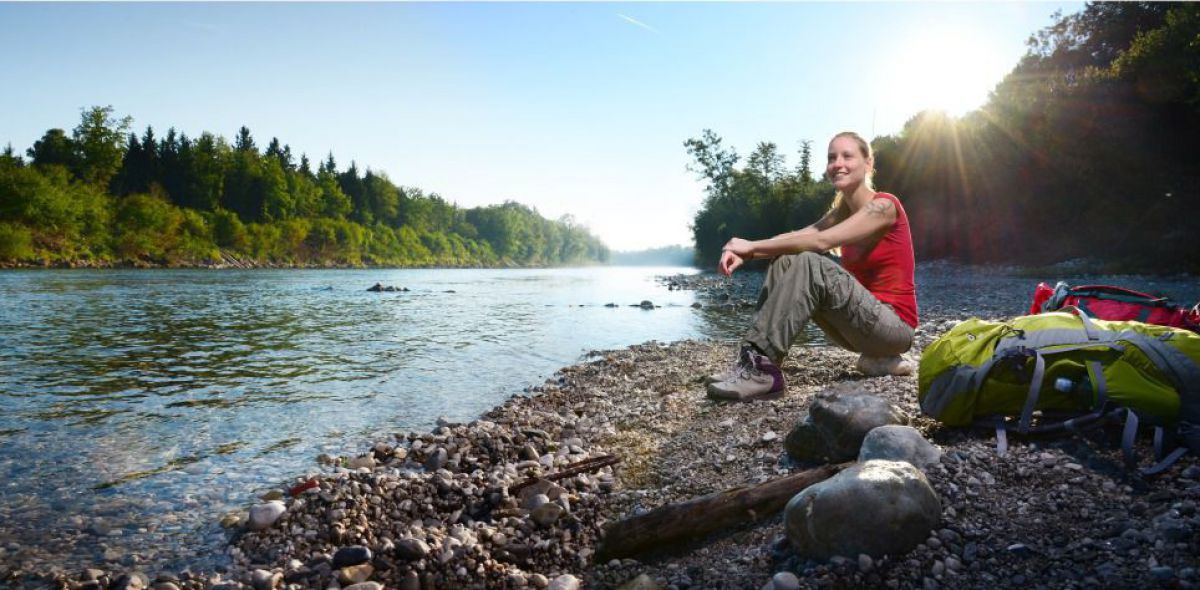 Frau sitzt auf einer Schtterbank am Ufer des Almflusses.