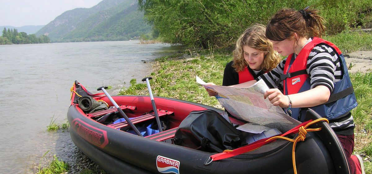 2 Mädchen mit einem Kanu am Ufer der Donau studieren eine Landkarte.