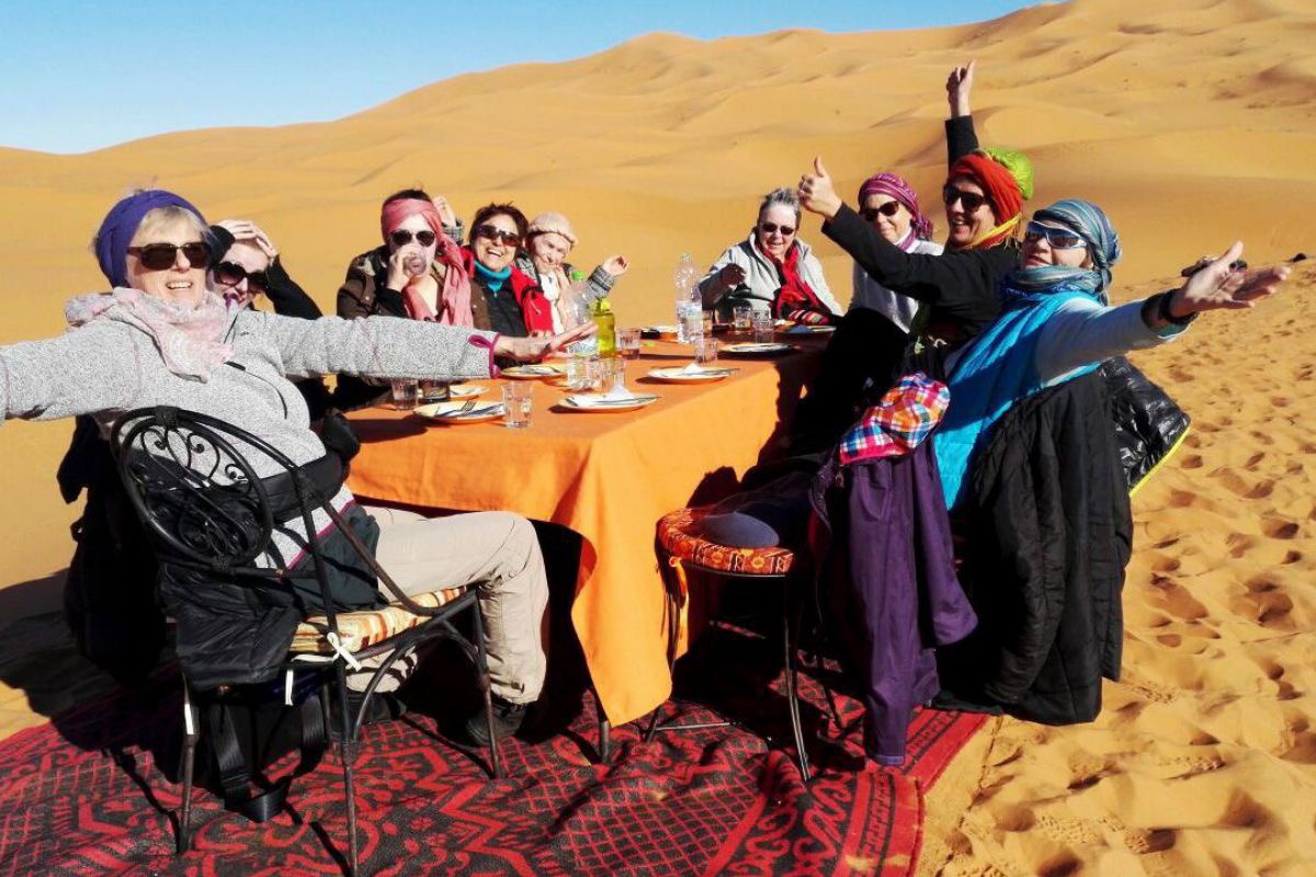 9 Frauen sitzen rund um einen Tisch in der marokkanischen Wüste.
