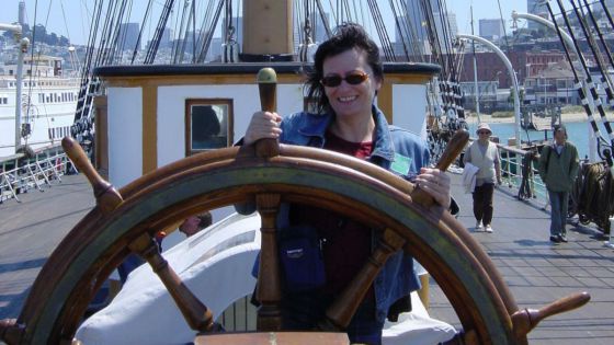 Frau am Steuerrad eines Segelschiffes.