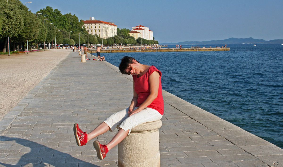 Frau sitzt auf einem Steinpoller im Hafen von Zadar.