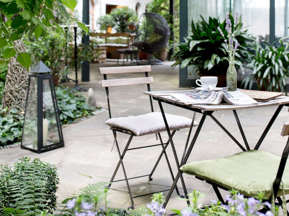 Tisch im Garten auf dem eine Kaffeetasse steht und eine aufgeschlagene Zeitung liegt