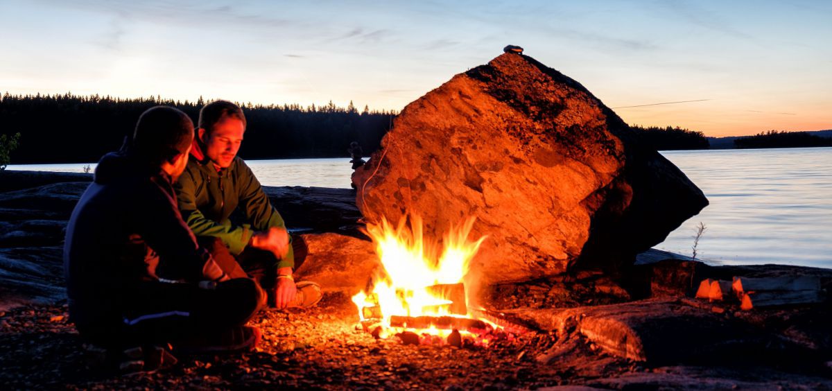 2 Männer am nächtlichen Lagerfeuer am See.