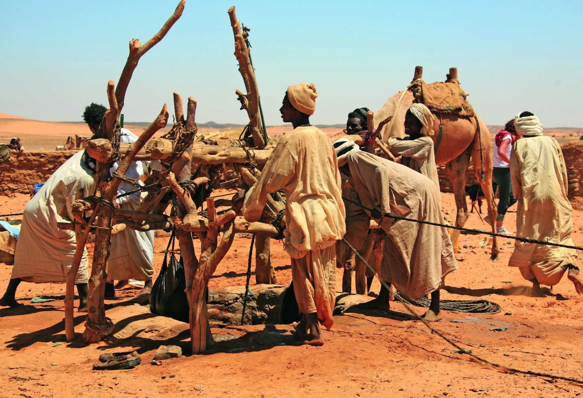 Männer rund um einen Brunnenloch in der Wüste ziehen an einem Seil Säcke mit Wasser hoch.