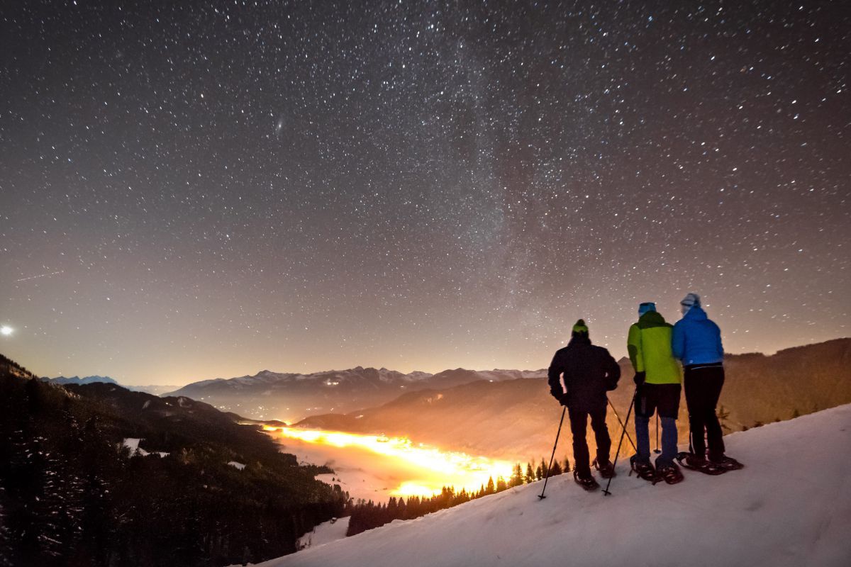 3 Schneeschuhwanderer in der Nacht unter einem beeindruckenden Sternenhimmel.
