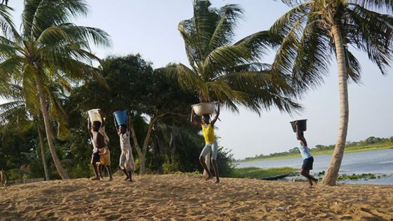 Frauen tragen Wasserkübel am Kopf, das sie aus dem Fluss geholt haben.