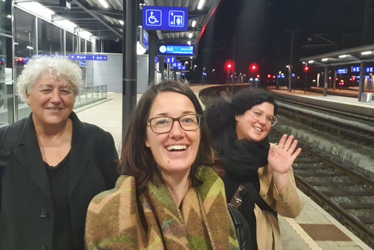 Drei Frauen stehen am Bahnhof und winken.