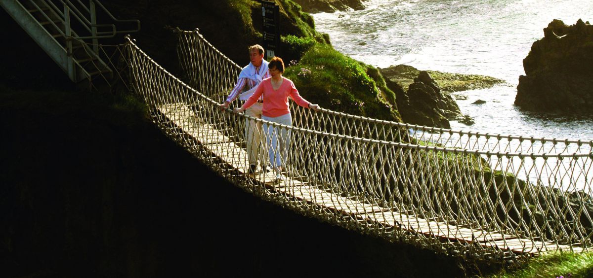 Mann und Frau gehen über eine Hängebrücke in den Klippen der Steilküste.