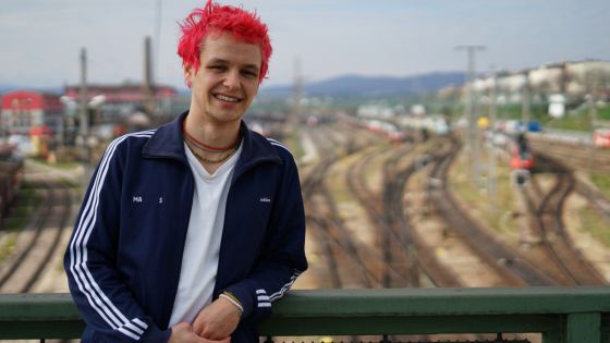 Elias Bohun mit rot gefärbten Haaren auf einer Brücke, darunter viele Geleise.