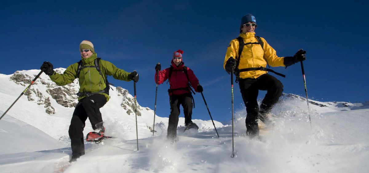 3 Personen stapfen mit Schneeschuhen ausgelassen durch den Schnee.