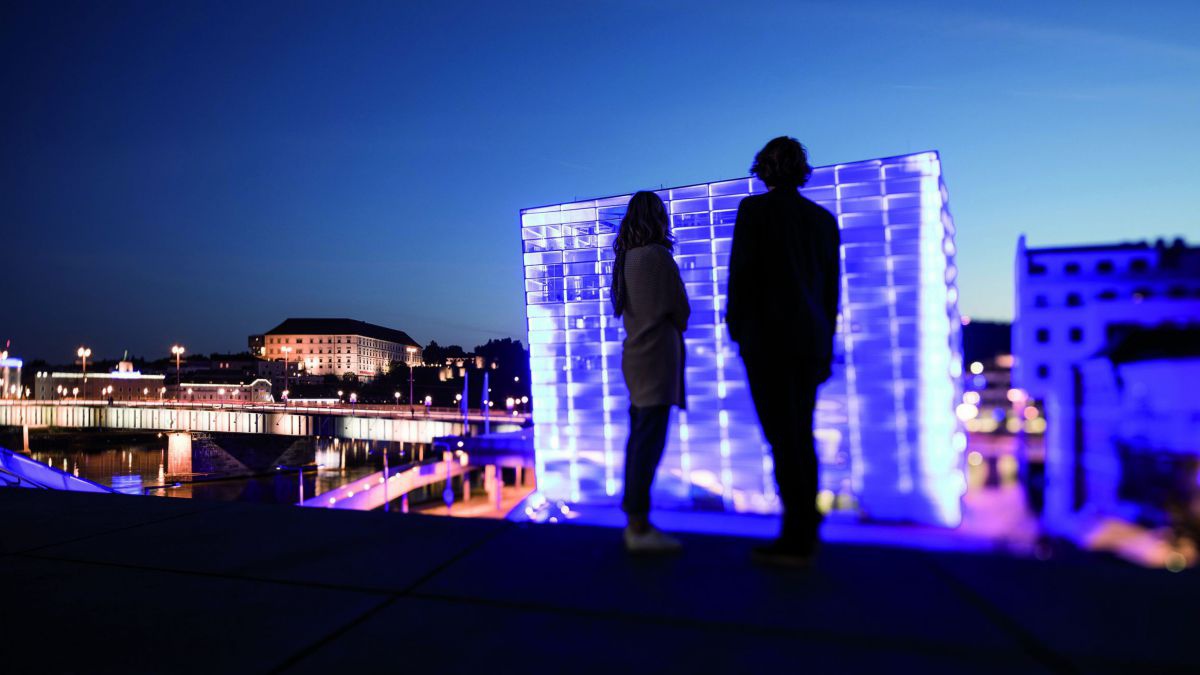 Mann und Frau als Silhuette vor einem beleuchteten Gebäude in der Nacht.