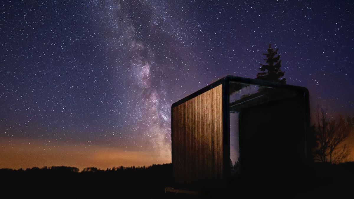 Einzeln stehendes Holzhaus in der Nacht, darüber die Milchstraße mit Millionen Sternen.