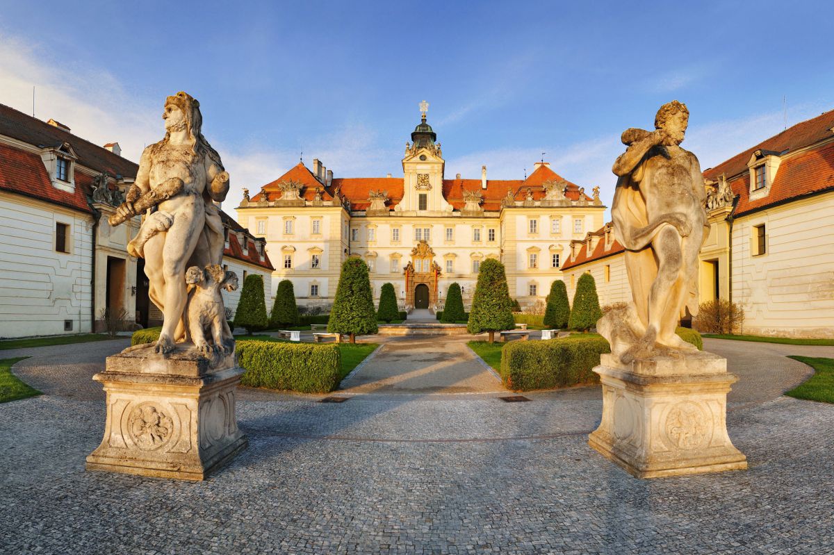 Eingang zum Schloss Valtice. 2 steinerne Statuen vpr einer runden Parlanlage - dahinter das Schloss.