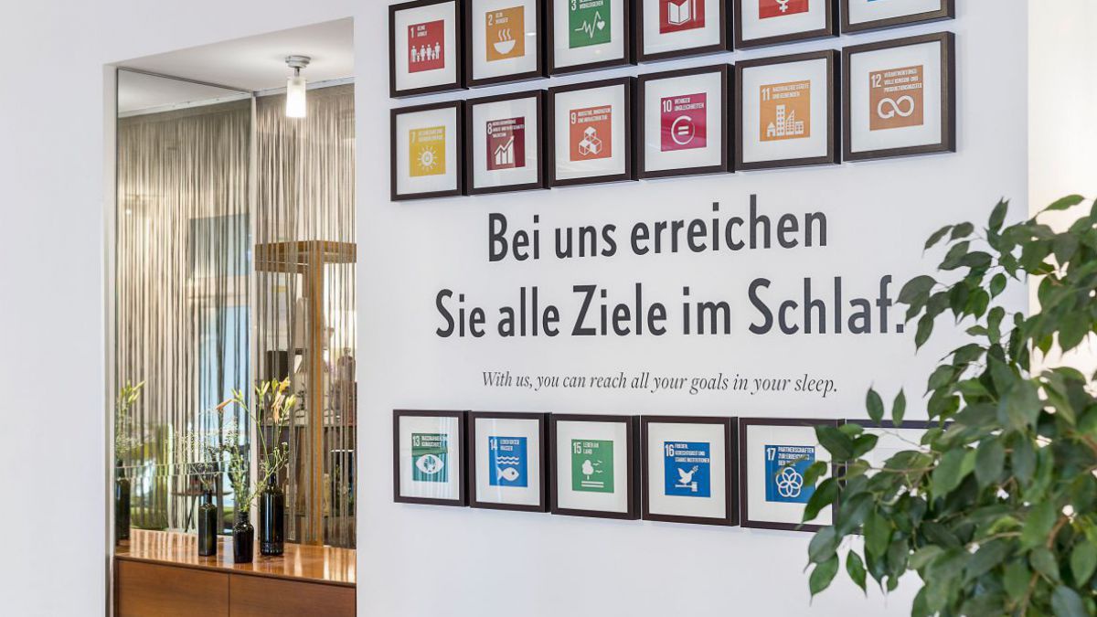 Lobby mit den Symbolen der 17 Nachhaaltigkeitszielen an der Wand. Dazu Textzeile: Bei uns erreichen Sie alle Ziele im Schlaf.