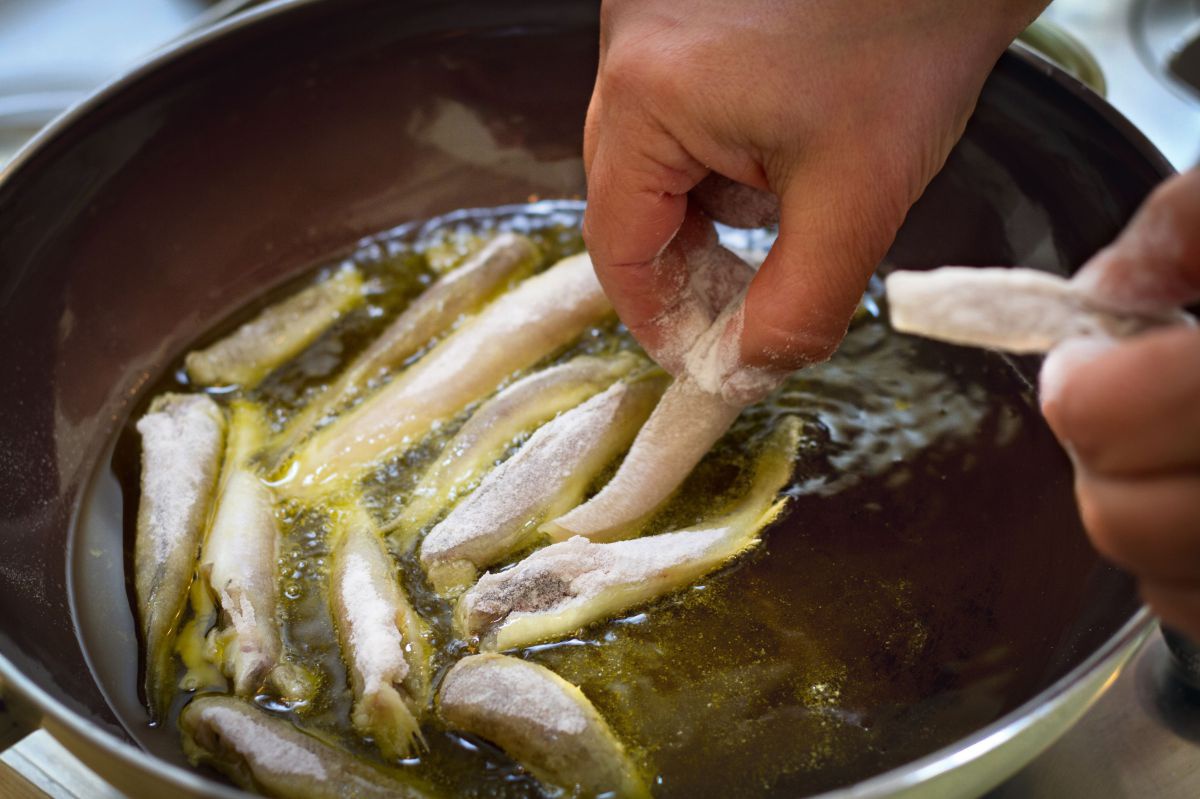 In Mehl gewälzte Sardinen werden von Hand in eine Pfanne mit Frittieröl gelegt.
