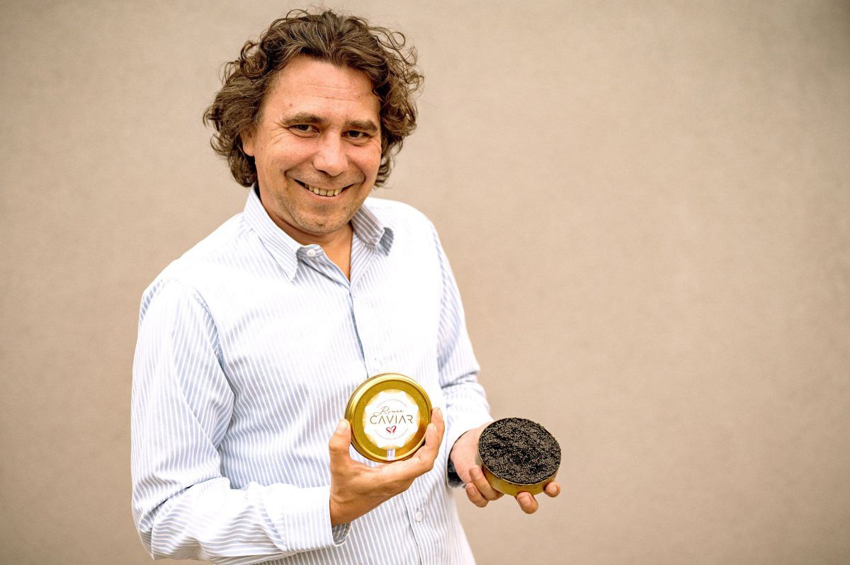 Ein Mann mit gelocktem braunen Haar hält lächelnd eine Dose seines Kaviars aus Eigenproduktion ins Bild.
