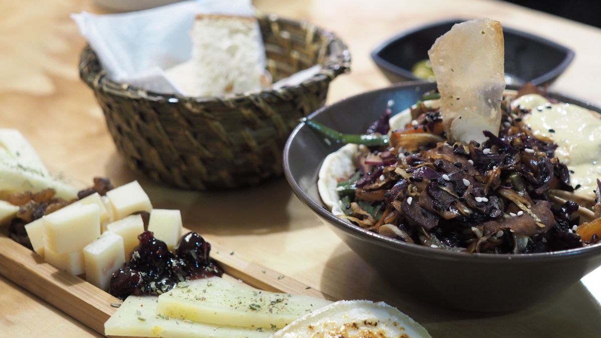 Tapas: Geschnittener Käse und Oliven auf einem Holzbrett, Salat in einer Schale, Weißbrotstücke in einem geflochtenen Körbchen angerichtet.