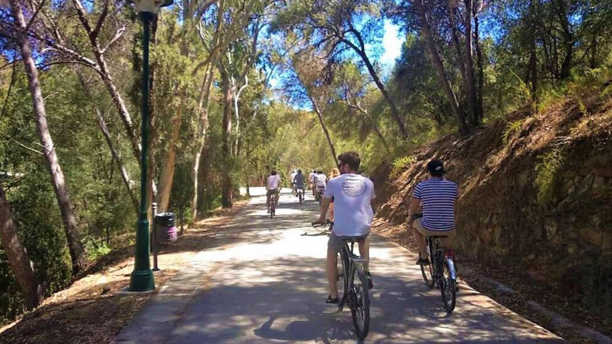 Radfahrer unterwegs auf einem Promenadenweg gesäumt von grünen Straßenlaternen, zahlreiche Bäume spenden Schatten an einem heißen Sommertag.