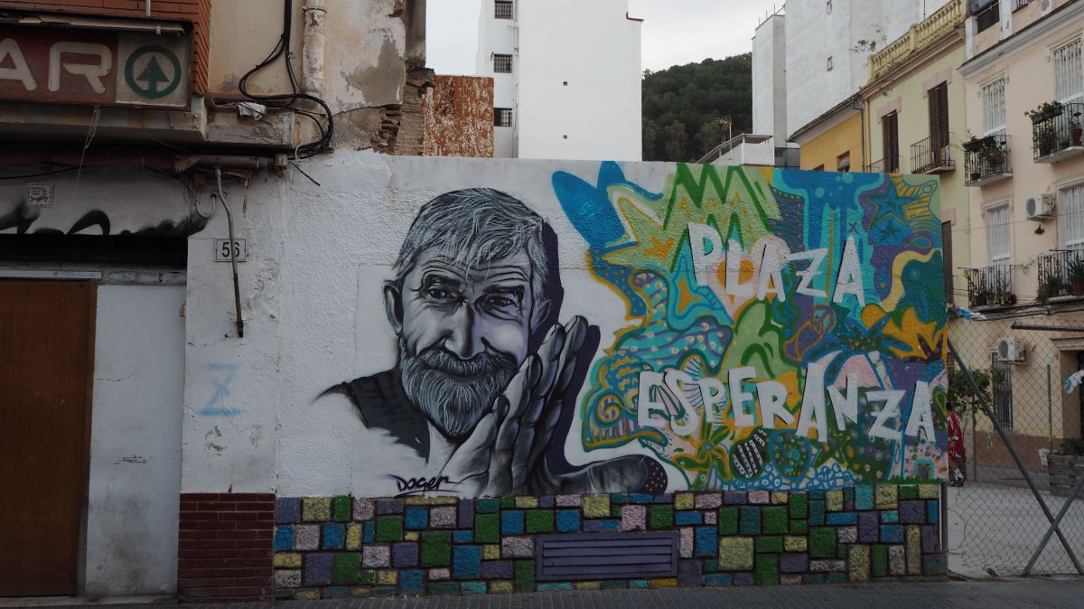 Eine Hauswand wurde mit bunter Straßenkunst verziert: Kopf und Hand eines lächelnden, bärtigen älteren Mannes, rechts daneben die Worte 