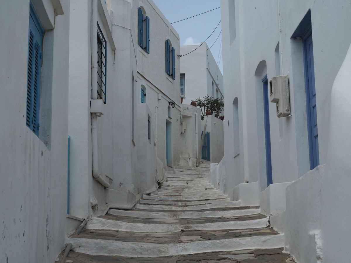 Eine enge steile Gasse zwischen weißen Häusern mit blauen Türen und Fensterläden.