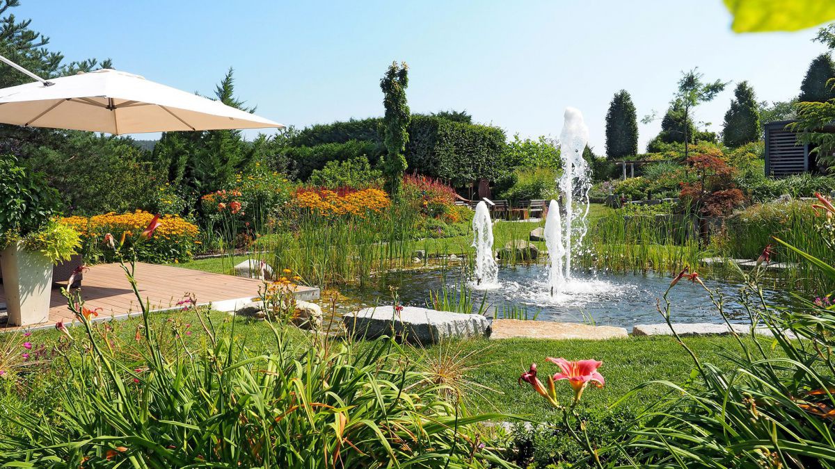 Garten mit Terasse, davor ein Teich mit Springbrunnen.